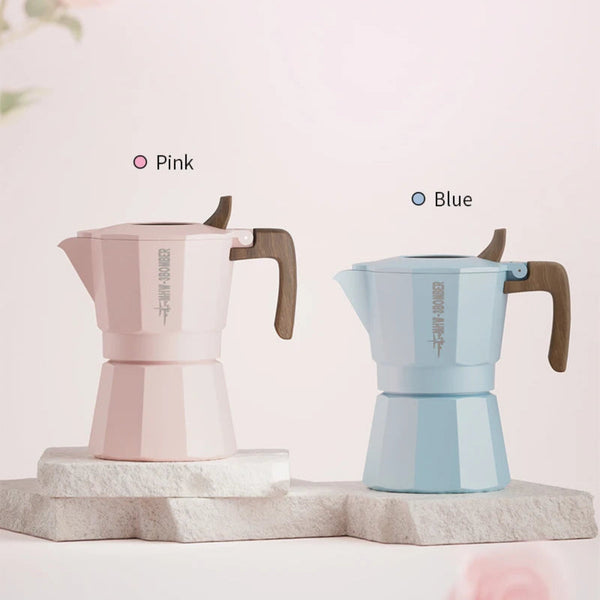 Two moka pots displayed side by side on a light stone pedestal against a soft pink background. The left pot is labeled Pink and is light pink with a brown handle.