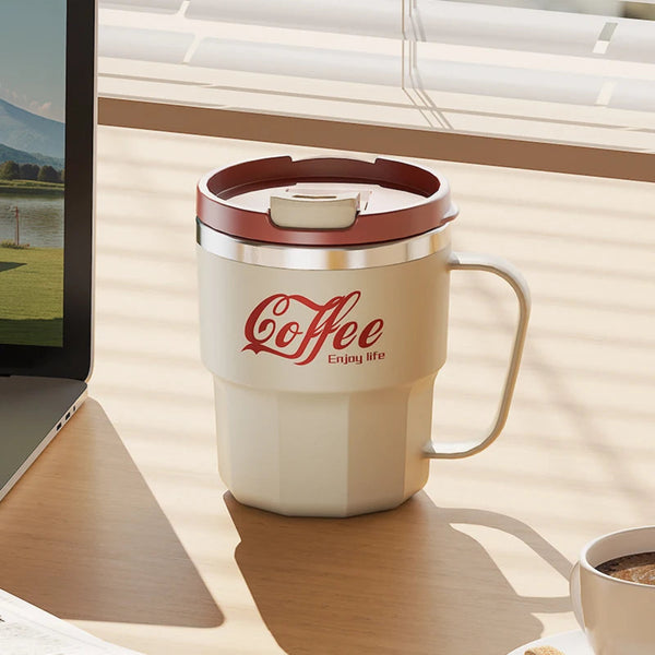 Beige insulated coffee mug with handle sitting on a wooden office desk next to a laptop