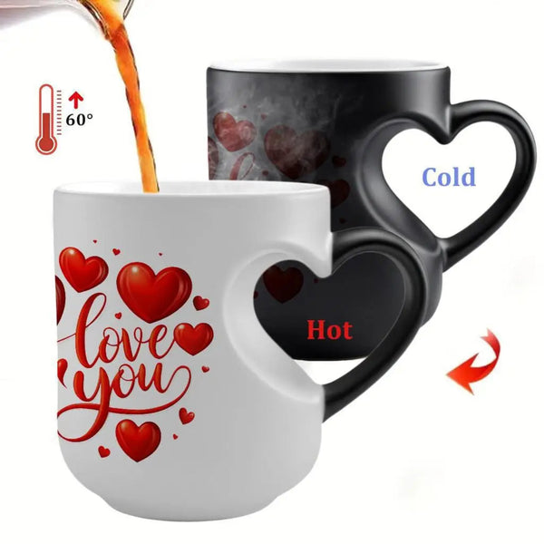 A white ceramic mug with a heart-shaped handle and red heart graphics, shown with an amber drink being poured into it. Behind it is a black version of the same mug that reveals red heart details when hot, with labels indicating cold and hot states.