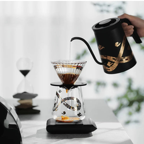 MHW-3BOMBER Serpent Series pour-over set with a black gooseneck kettle pouring water into a glass V60 dripper and coffee server.