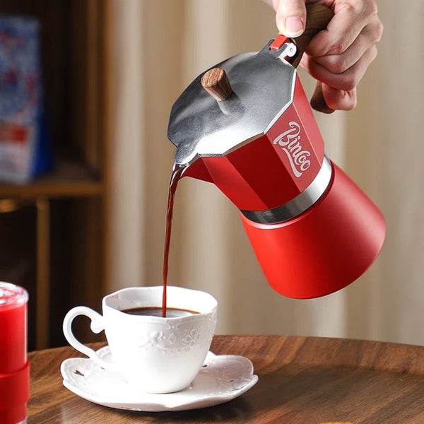 Red coffee maker pouring coffee into a white cup on a wooden table.