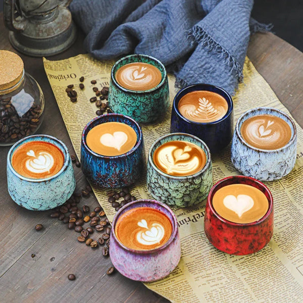Assorted minimalist kiln-glazed ceramic coffee cups in green, white, blue, and red variants filled with latte art.