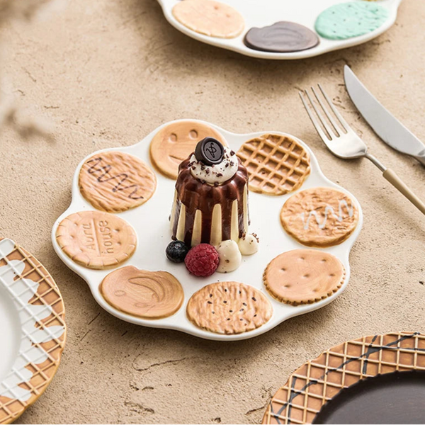 White scalloped ceramic dessert plate with 3D miniature cookie decorations and waffle patterns featuring a chocolate cake and berries.