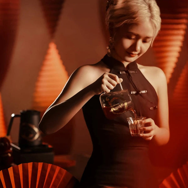A barista pouring fresh coffee from an MHW-3BOMBER Serpent Series Glass Server into a matching glass cup against a warm, artistic background.