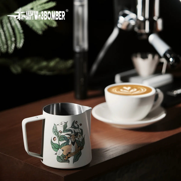 MHW-3BOMBER Origin Series milk pitcher on a wooden coffee station next to a latte with professional art.