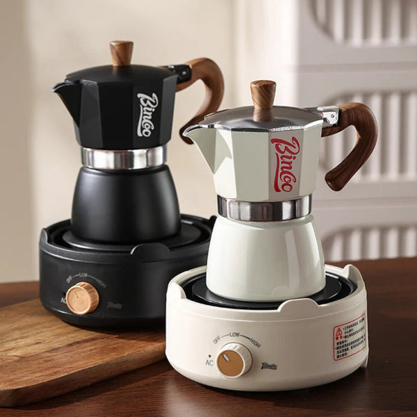 Two Bincoo moka pot coffee makers on electric stovetops, one in matte black and one in cream and silver, displayed on a wooden table.