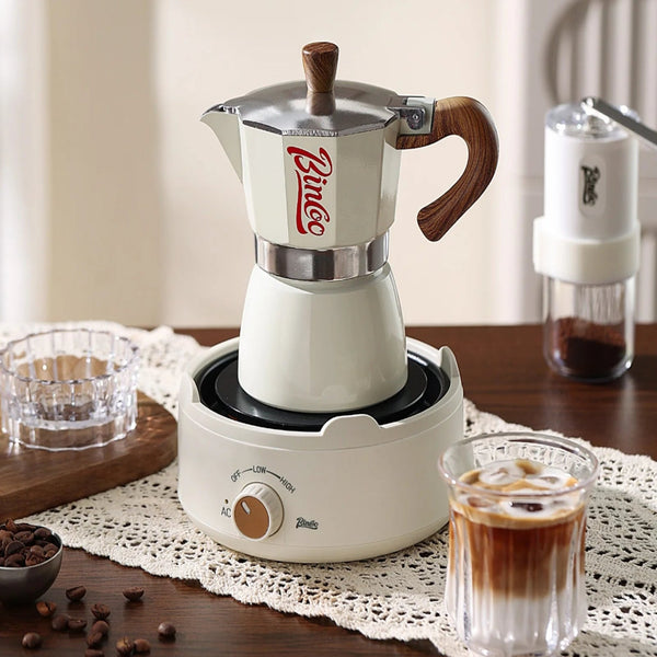 Bincoo coffee maker on a wooden table with a glass of coffee and coffee beans.