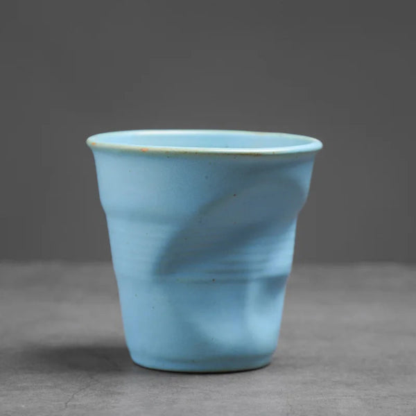 Serene blue crumpled ceramic espresso cup with a hand-pinched pleated texture on a grey background.