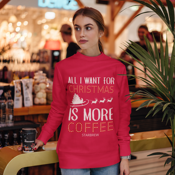 A woman wearing a vibrant red Gildan 18000 Christmas sweatshirt that reads "All I want for Christmas is more coffee, Starbrew" inside a cozy coffee shop setting.
