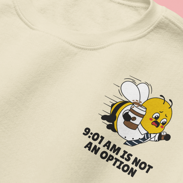 Close-up detail of the left chest embroidery on the oatmeal cream crewneck sweatshirt, showing a funny cartoon bee rushing with a coffee cup and the bold text "9:01 AM IS NOT AN OPTION."