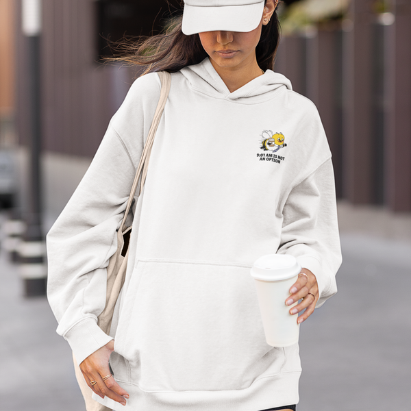 A woman walking outdoors holding a coffee cup, wearing an oversized Ceramic White unisex streetwear hoodie featuring a small left-chest embroidered design of a running corporate bee mascot and the text slogan 9:01 AM IS NOT AN OPTION.