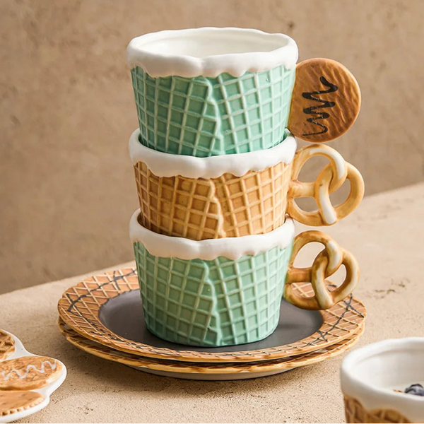 Stacked mint green and tan waffle texture ceramic mugs with creative cookie and pretzel shaped handles on matching biscuit plates.
