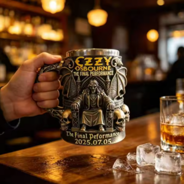 A hand holding a 3D Ozzy Osbourne gothic skull tankard over a wooden bar counter with ice cubes and a glass of whiskey.