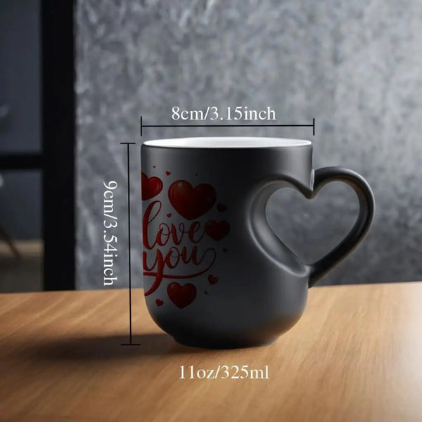 A dark gray ceramic mug with a heart-shaped handle and 'love you' printed in red on the side, shown on a wooden table with dimension lines indicating 8cm width, 9cm height, and 11oz capacity.