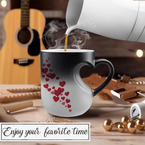 A heart-shaped ceramic mug with a black-to-white gradient and red heart pattern, shown with coffee being poured into it. The mug is set on a wooden table with a guitar and other warm-toned background elements, and the text 'Enjoy your favorite time' appears at the bottom.