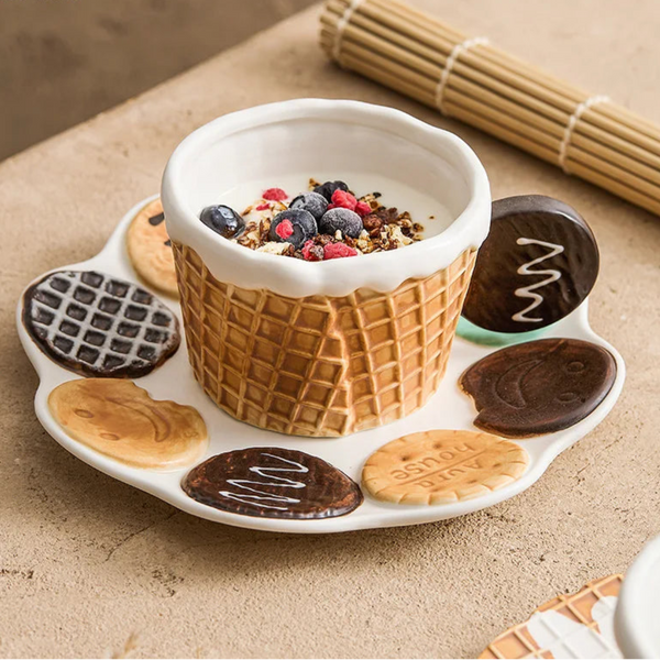 Tan waffle-textured ceramic bowl with a chocolate cookie handle sitting on a white scalloped plate decorated with 3D chocolate and butter biscuits.