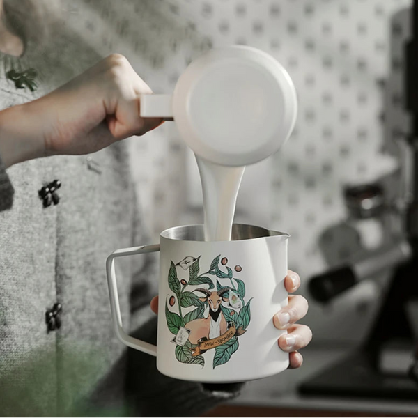 Hand transferring milk into an MHW-3BOMBER Origin Series pitcher for professional latte art preparation.