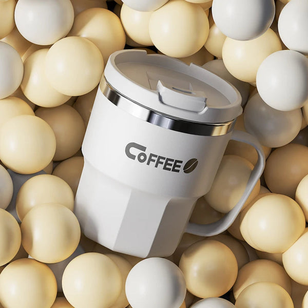White insulated stainless steel coffee mug with handle resting on a bed of cream aesthetic spheres