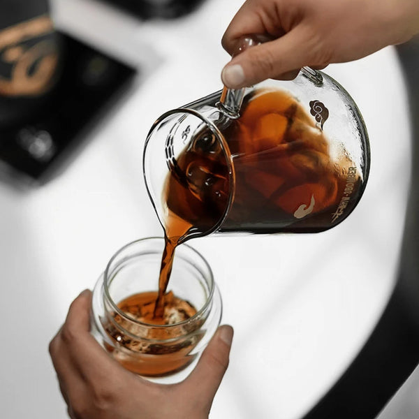 Barista pouring coffee from an MHW-3BOMBER Serpent Series Glass Server into a double-walled glass cup, showcasing the precision spout.