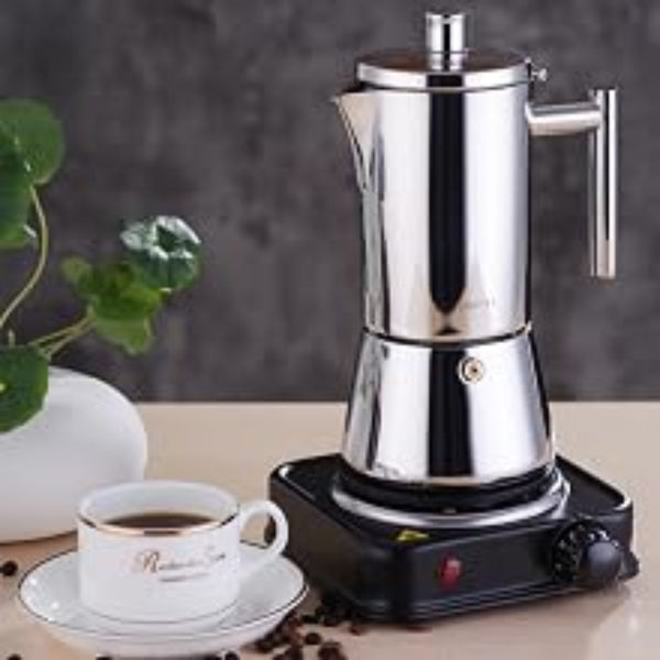 Stainless steel moka pot on a small electric hot plate with a cup of coffee and coffee beans.