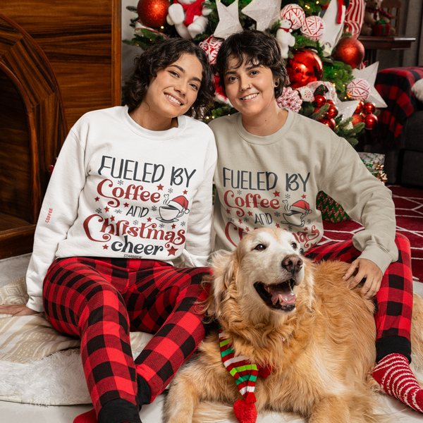 Two people wearing matching Fueled by Coffee and Christmas Cheer sweatshirts with a golden retriever dog by a decorated holiday tree.