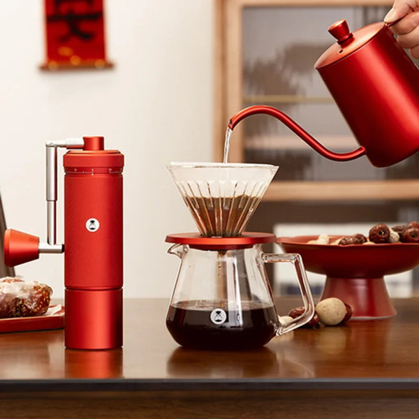 TIMEMORE Chestnut S3 Red manual coffee grinder standing next to a matching red gooseneck kettle pouring hot water into a glass pour-over dripper and server on a wooden table.